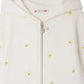 Close-up of the Bonpoint Girls' Talent Hoodie, a zip-up sweatshirt made from organic cotton fleece, adorned with delicate cherry embroidery on soft white fabric.