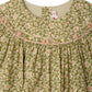 Close-up of the Bonpoint Baby Girls' and Girls' Amantine Smocked Dress, showing a floral print and pink and yellow hand-embroidered smocking at the neckline, with the label visible inside the collar.
