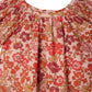 Close-up of Bonpoint's Baby Girls' and Girls' Carmella Smocked Dress in pink with a red, orange, and white floral Liberty print, featuring smocked details at the neckline and gathered shoulders.