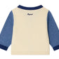 The Bonpoint Baby Boys' Tahiel V-neck Cardigan is cream-colored with blue sleeves and collar, made from organic cotton, and has "Bogesi" embroidered on the back near the neckline.
