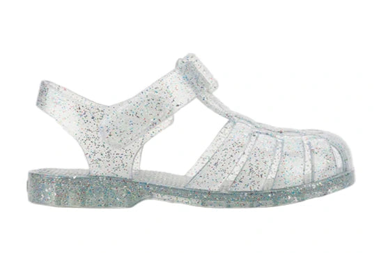 The Igor Clasica Cristal Sandal is a flexible, clear jelly sandal with silver glitter, a closed toe, ankle strap, and flat sole.