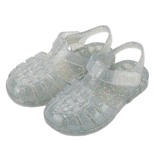 The Igor Clasica Cristal Sandal is a pair of flexible, translucent glitter jelly shoes with closed toes and ankle straps, shown on a white background.