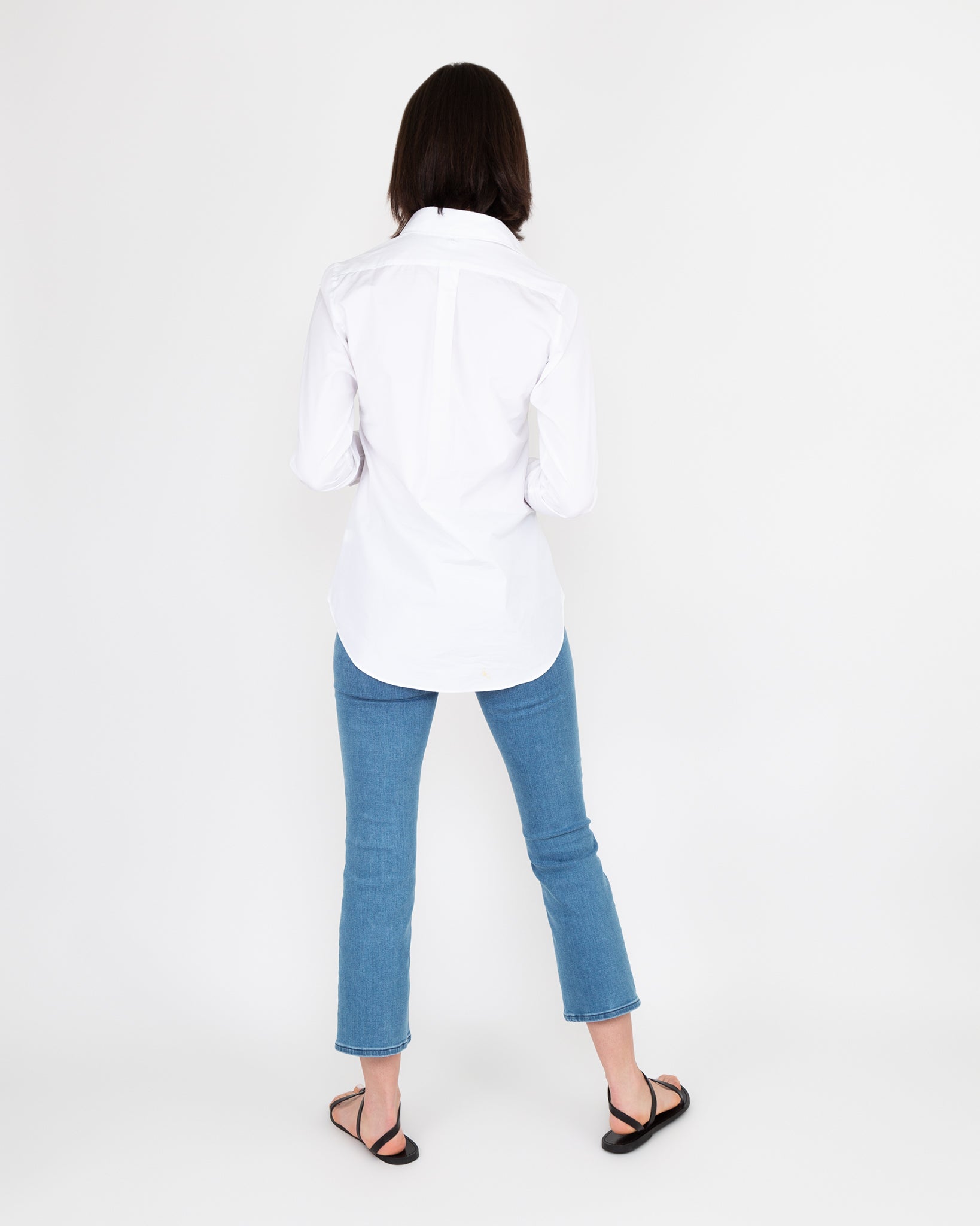 Woman standing with her back to the camera wearing an Ann Mashburn Boyfriend Shirt, blue jeans, and black sandals.