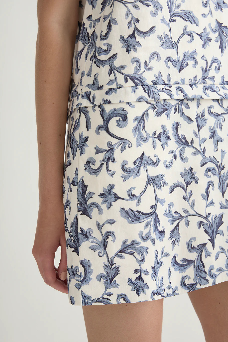 Wearing the POSSE Rue Shift Dress, featuring a blue floral pattern on white, only the lower torso, hip, and part of the arm are visible against a plain background.