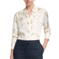A woman wears the Altuzarra Chika Top, a relaxed white button-up with a subtle floral print and long cuffed sleeves, tucked into high-waisted dark trousers.