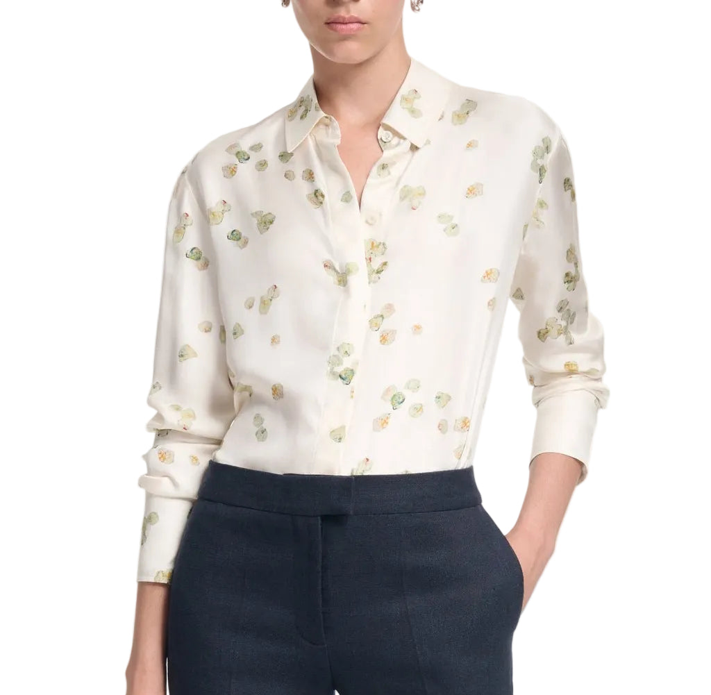 A woman wears the Altuzarra Chika Top, a relaxed white button-up with a subtle floral print and long cuffed sleeves, tucked into high-waisted dark trousers.
