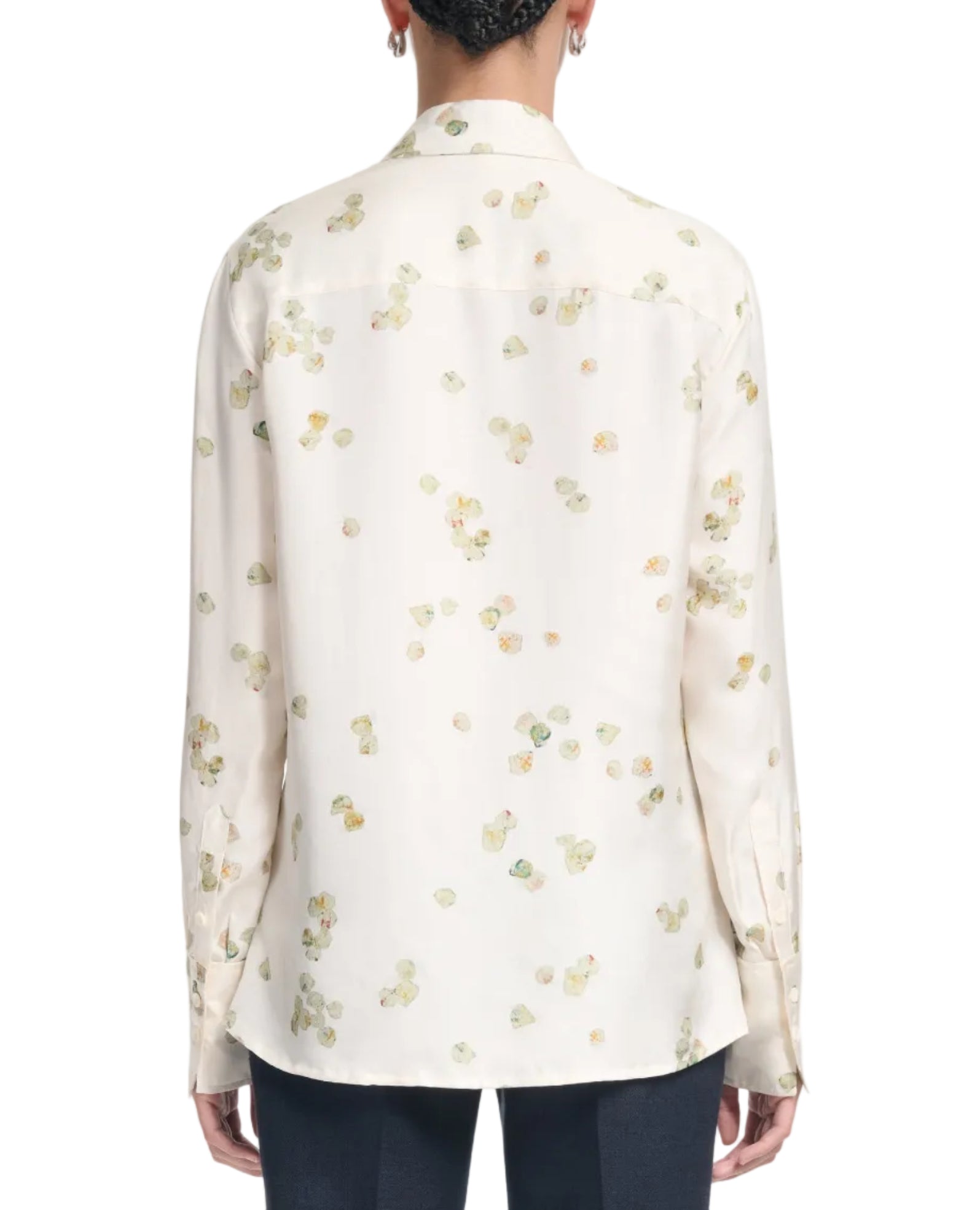 A person wearing the Altuzarra Chika Top, a relaxed silk blouse with long cuffed sleeves and a light floral pattern, shown from the back.
