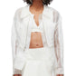 A person wearing a 3.1 Phillip Lim Organza Belted Flounce Jacket over a white crop top and skirt stands against a plain background, effortlessly embodying smart casual style.