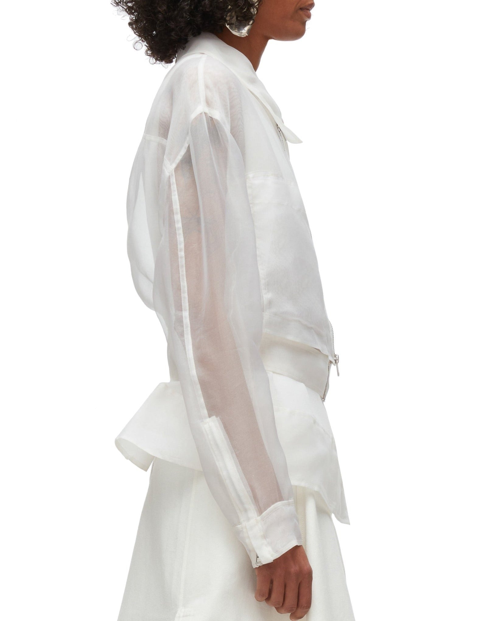 A side profile of a person wearing a sheer white long-sleeve shirt, a white skirt, and an elegant 3.1 Phillip Lim Organza Belted Flounce Jacket by 3.1 Phillip Lim.