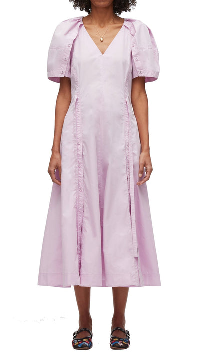 A person wearing a light pink 3.1 Phillip Lim Bloom Sleeve V-Neck Dress with voluminous sleeves and a V-neckline, standing with arms at their sides. The dress has vertical seam details and is paired with colorful sandals.