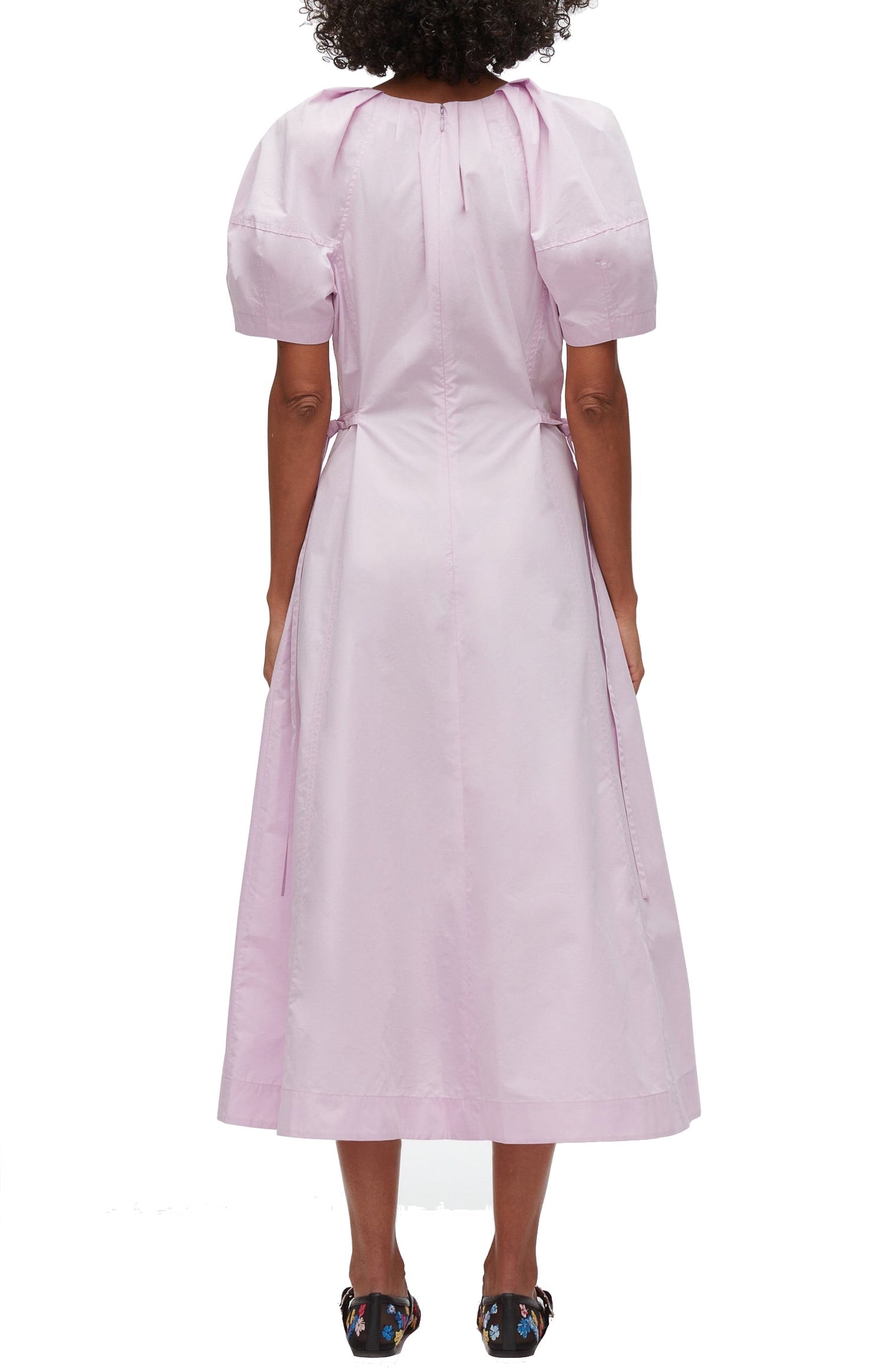 A person wearing a light pink, short-sleeved 3.1 Phillip Lim Bloom Sleeve V-Neck Dress by 3.1 Phillip Lim, shown from the back. The dress has a tie detail at the neck and a seam at the waist. The individual is standing with their back to the camera, highlighting the elegance of this Japanese poplin creation.