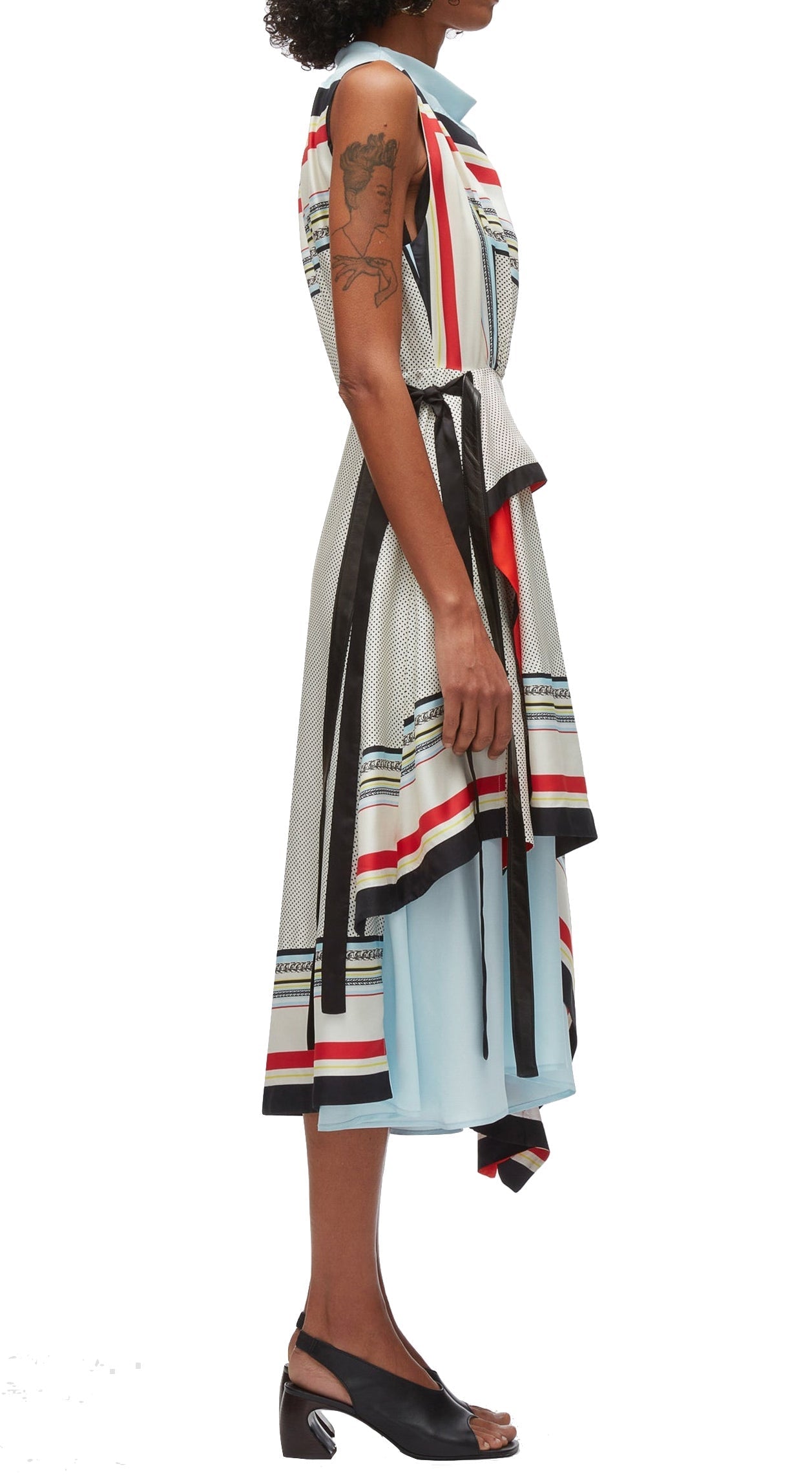 A person wearing a sleeveless 3.1 Phillip Lim Liberty Cascade Dress with vertical stripes and a belt stands sideways. The dress features a cowl neckline and an asymmetric hem. The person has a tattoo on their upper arm and is wearing black open-toe heels.