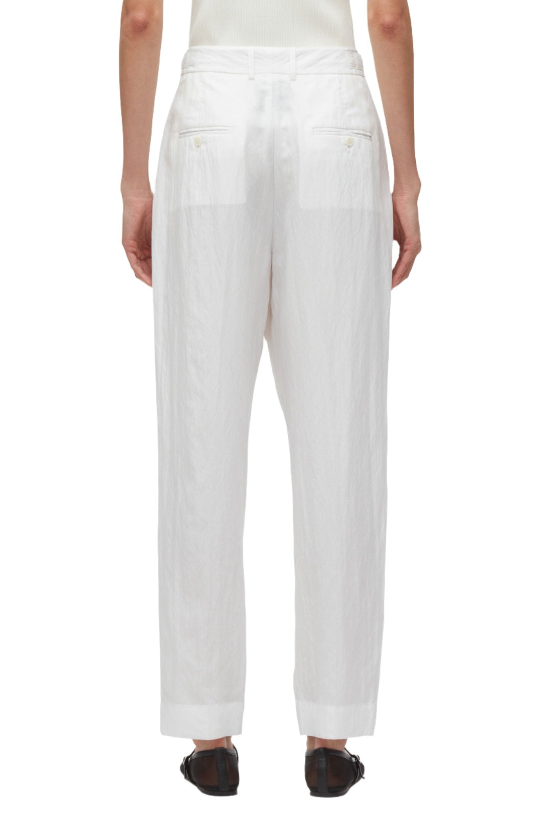 Person wearing loose-fitting 3.1 Phillip Lim Double Pleated Tapered Trouser, made of soft white poplin, viewed from the back, showcasing the waist and leg details with a touch of elegance. Paired with dark shoes, these trousers create a refined yet relaxed look.