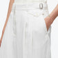 Person wearing 3.1 Phillip Lim Double Pleated Tapered Trouser in white, paired with a sleeveless top. They have one hand in their pocket, and a small tattoo is visible on their wrist.