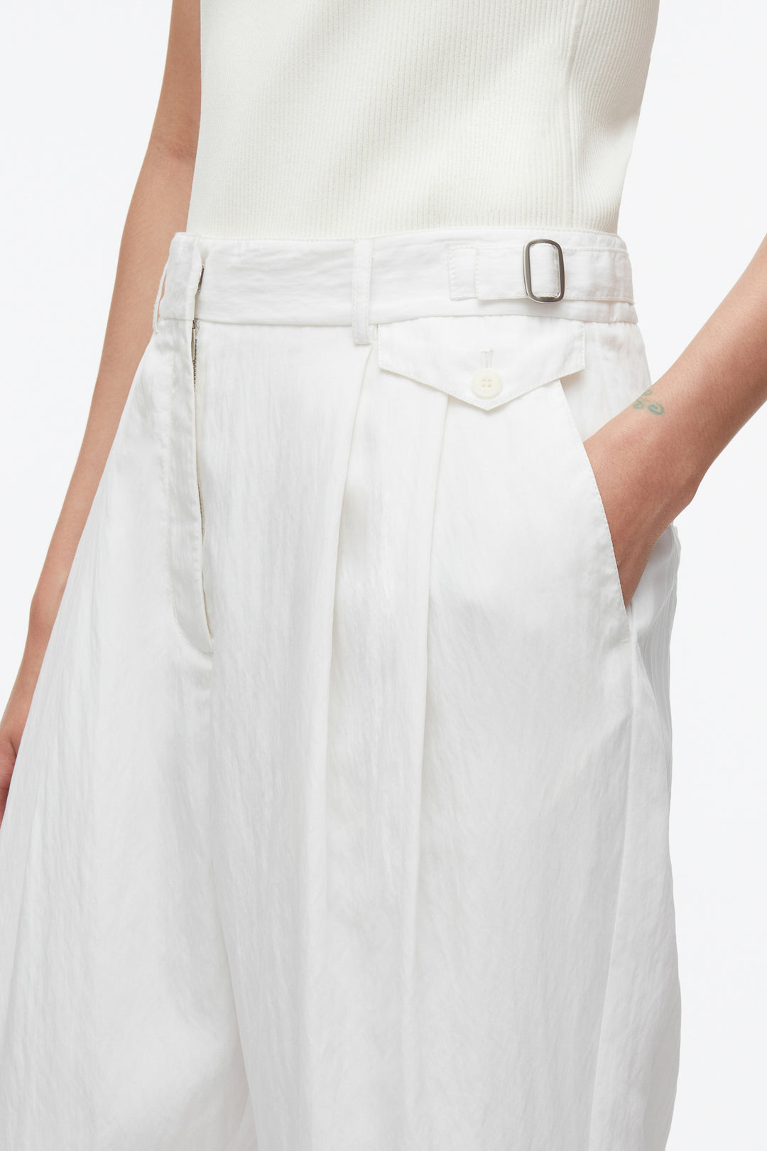 Person wearing 3.1 Phillip Lim Double Pleated Tapered Trouser in white, paired with a sleeveless top. They have one hand in their pocket, and a small tattoo is visible on their wrist.