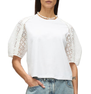 A woman stands with one hand in her pocket, wearing the 3.1 Phillip Lim Broderie Anglaise Combo T Shirt, blue jeans, and a pearl necklace.