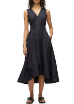 A woman wears the Crisscross Back Midi Dress by 3.1 Phillip Lim—a sleeveless, V-neck style with a black belted A-line skirt in technical poplin, asymmetrical hem, and paired with black sandals.