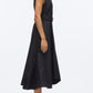 A woman stands in profile wearing the 3.1 Phillip Lim Crisscross Back Midi Dress, a sleeveless black A-line with a belted waist and V-neck, styled with black sandals against a plain white background.
