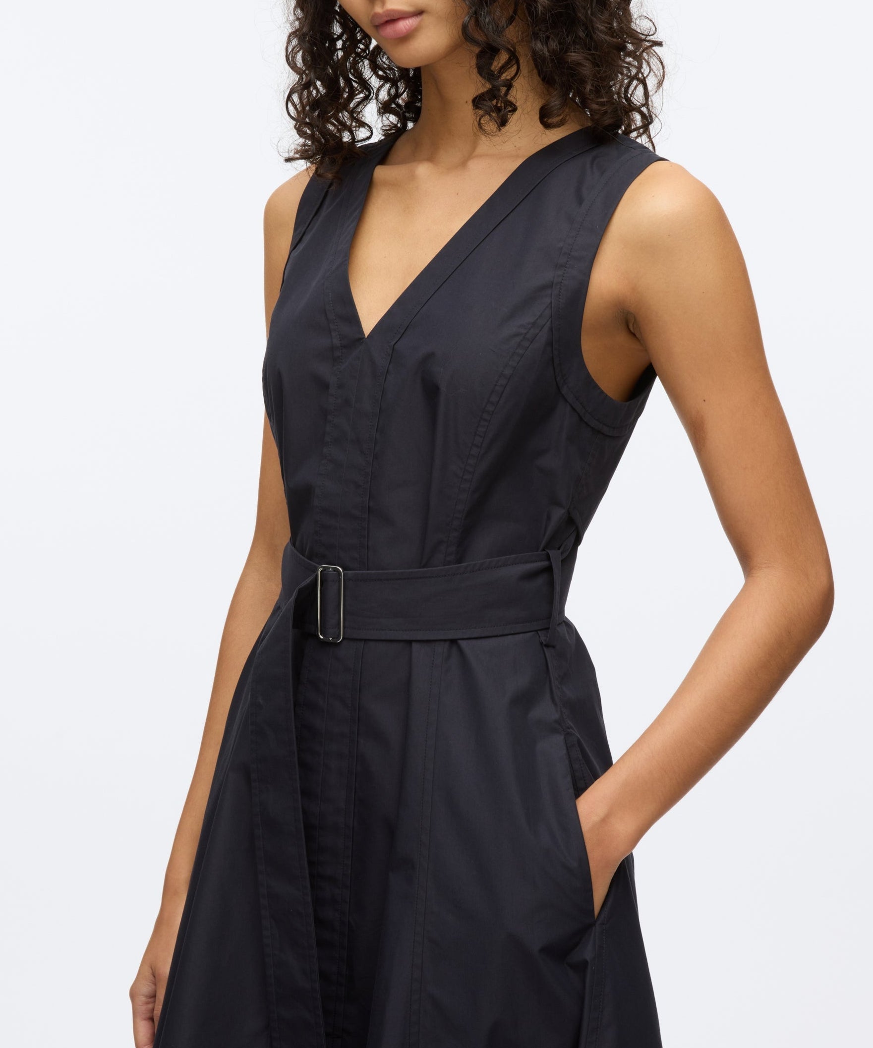 A woman models the 3.1 Phillip Lim Crisscross Back Midi Dress, featuring a sleeveless V-neck, belted waist, A-line skirt in technical poplin, and side pocket, shown from shoulders to above the knee.