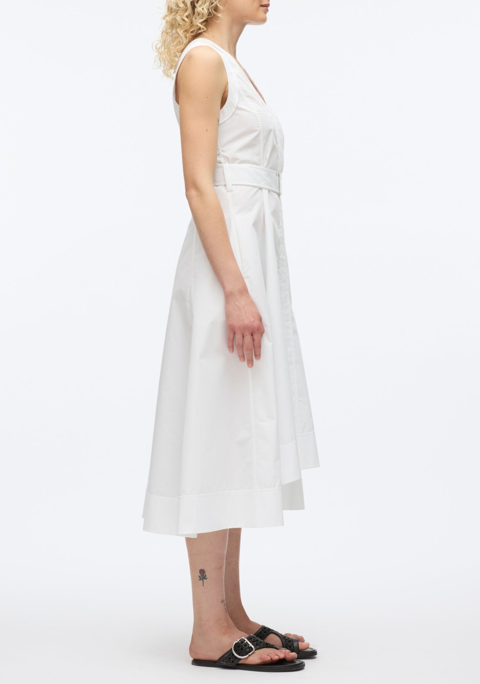 A woman stands in profile against a plain white background wearing the 3.1 Phillip Lim Crisscross Back Midi Dress with a V-neck, A-line skirt, and black sandals.