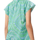 A woman is seen from the back wearing the Fia Top by Figue, a green piece with blue and white patterns. Its short sleeves and V-neckline pair perfectly with her blue jeans.