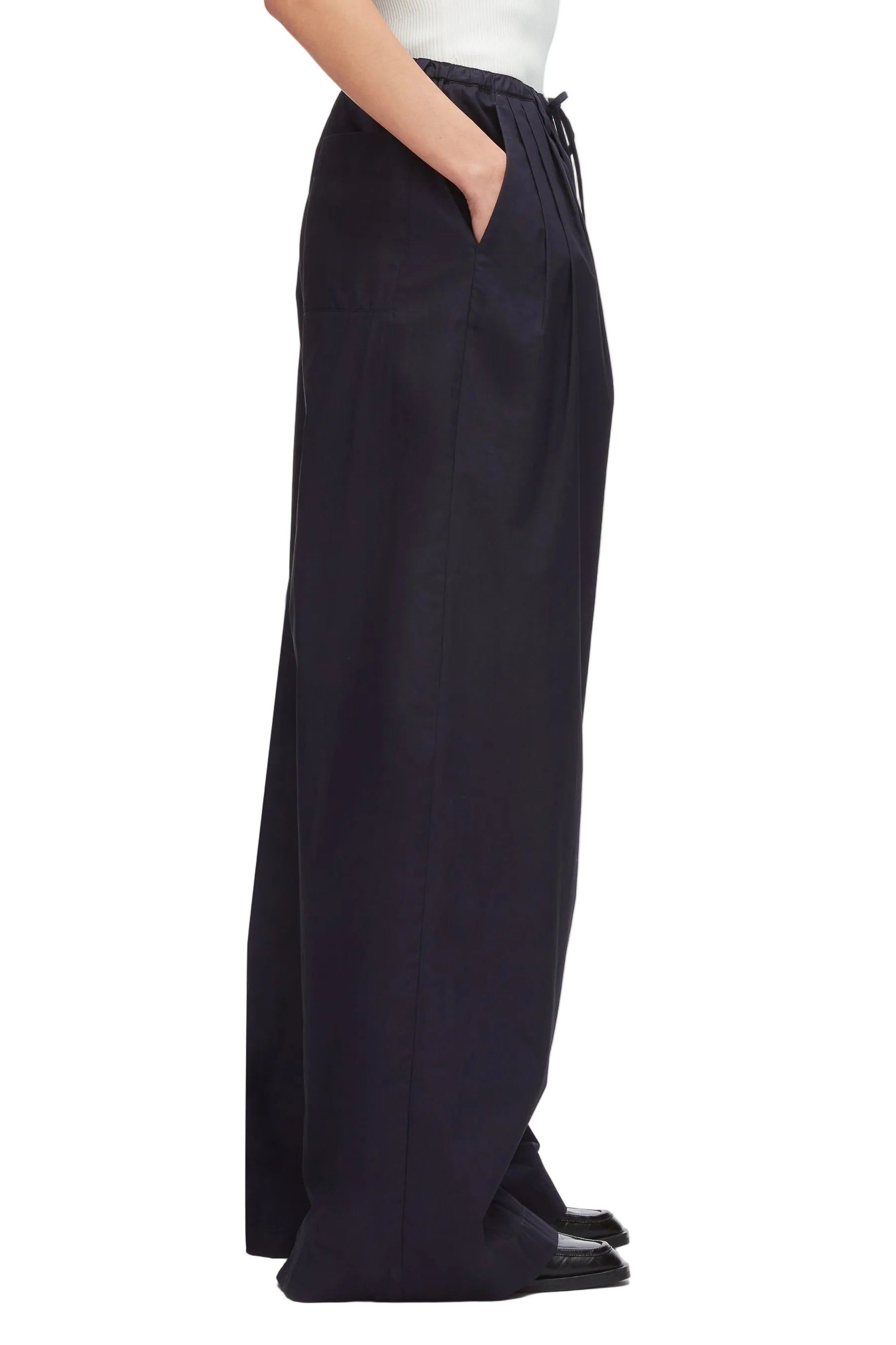 A person wears 3.1 Phillip Lim Structured Cotton Pull-On Straight Leg Pants in black, featuring side pockets and a drawstring waist, crafted from cotton poplin; shown standing sideways, visible from chest down.