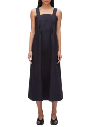A person wears the 3.1 Phillip Lim Structured Cotton Poplin Midi Dress—sleeveless, ankle-length, dark navy with wide shoulder straps—paired with black shoes, standing against a plain white background.