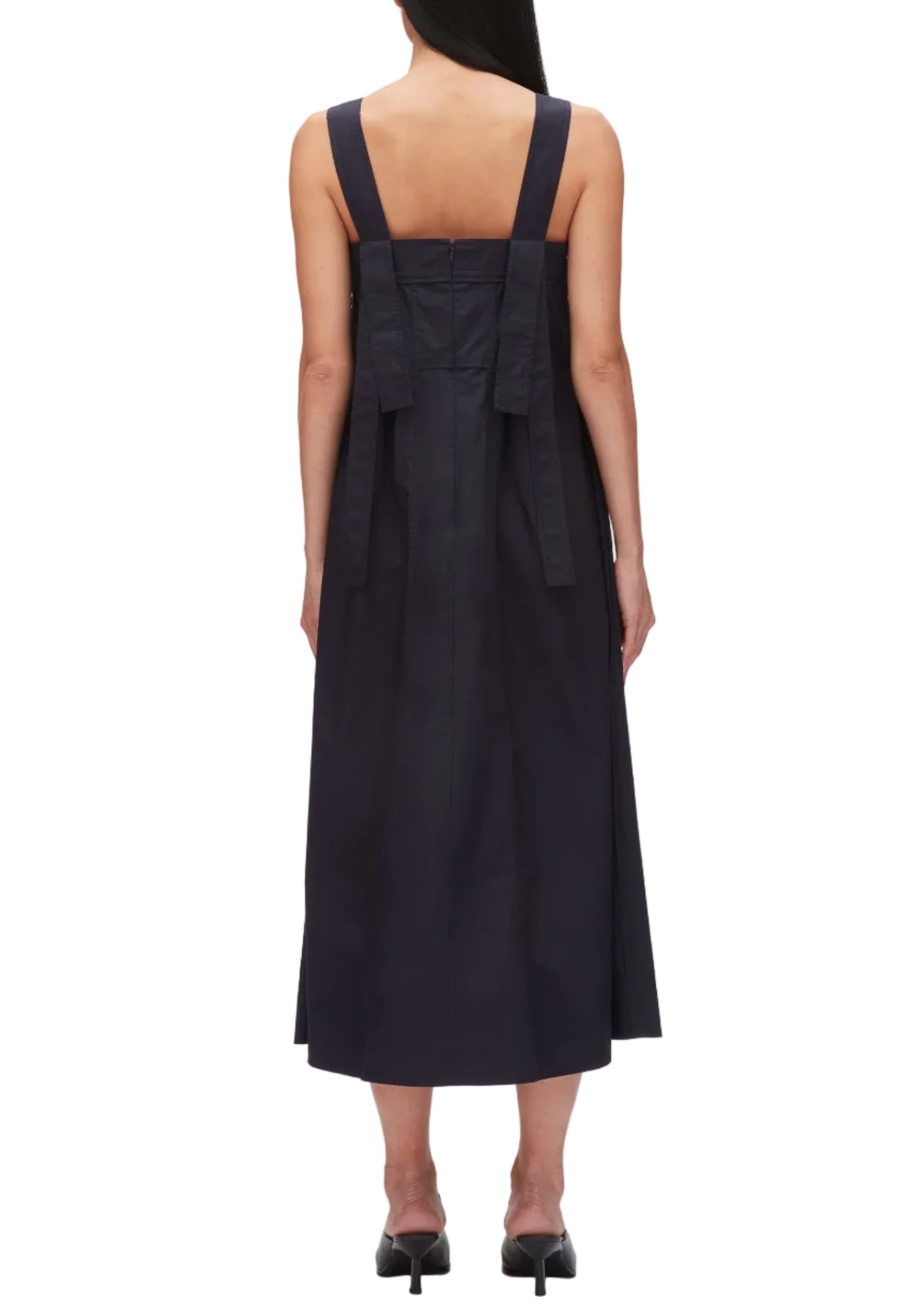 A woman is seen from the back wearing the 3.1 Phillip Lim Structured Cotton Poplin Midi Dress with wide straps, a bow detail, and a square neckline, styled with black heeled shoes.