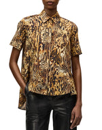 Someone wears the Adam Lippes Charlie Top—a collared style with a brown, black, and gold abstract pattern—paired with black leather pants.