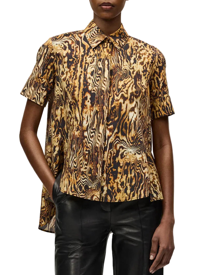 Someone wears the Adam Lippes Charlie Top—a collared style with a brown, black, and gold abstract pattern—paired with black leather pants.