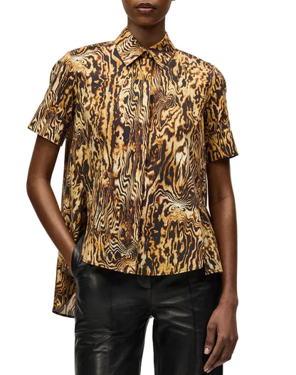 Someone wears the Adam Lippes Charlie Top—a collared style with a brown, black, and gold abstract pattern—paired with black leather pants.