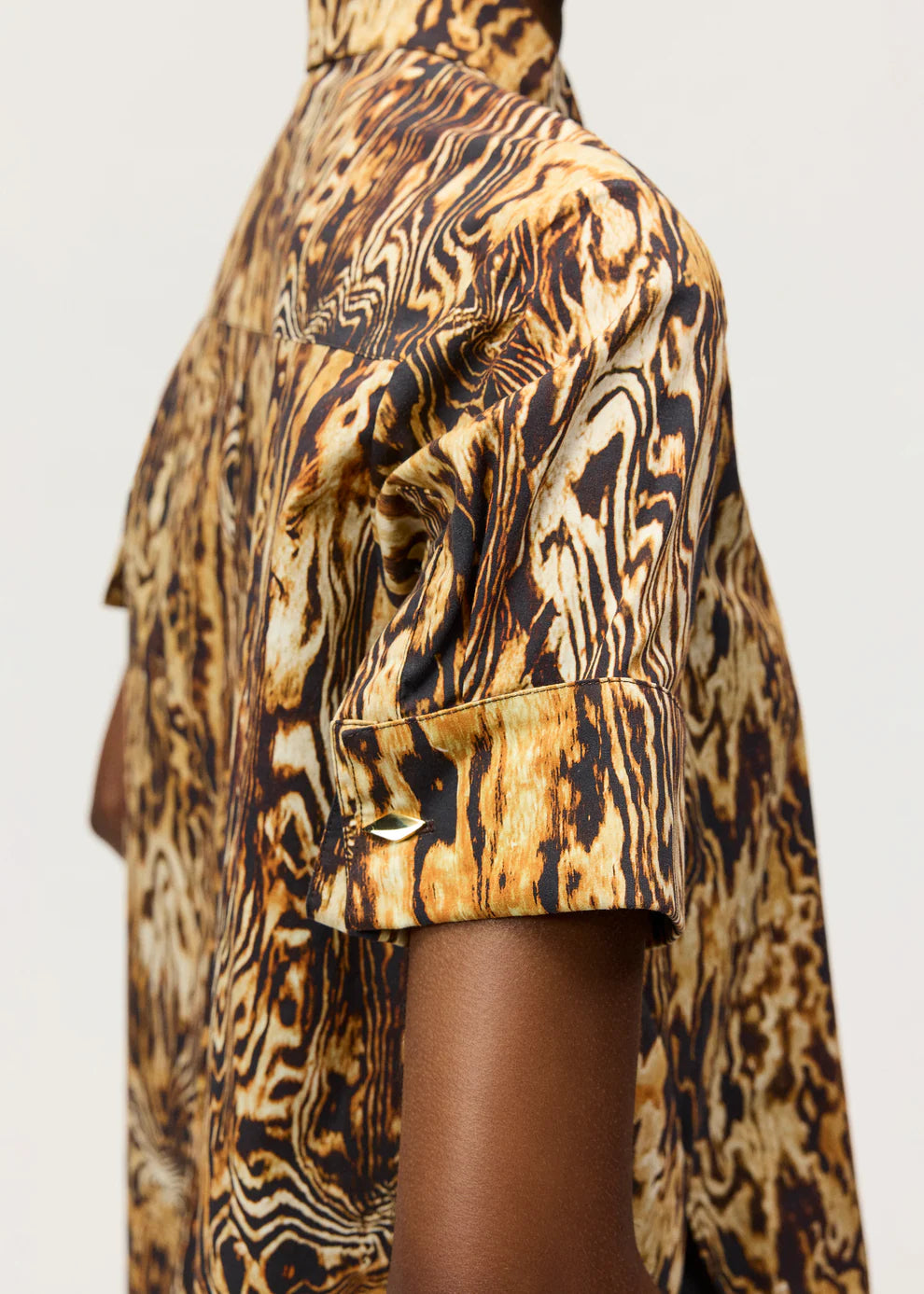 Wearing the Adam Lippes Charlie Top, a short-sleeved, collared shirt with a brown, black, and tan abstract wavy pattern; sleeves are rolled up and fastened with buttoned tabs.