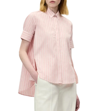 A person wearing the Adam Lippes Charlie Top, a pink and white striped collared blouse with a high-low hem, paired with white trousers.