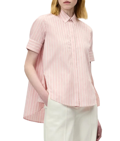 A person wearing the Adam Lippes Charlie Top, a pink and white striped collared blouse with a high-low hem, paired with white trousers.