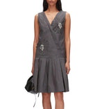 A woman stands against a white background wearing the 3.1 Phillip Lim Draped Tank Dress with Floral Applique, a sleeveless gray knee-length wrap dress adorned with floral appliqué and bead details, and holding a black handbag.
