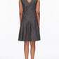 A woman stands facing away, wearing the 3.1 Phillip Lim Draped Tank Dress with Floral Applique—a sleeveless gray knee-length dress featuring a V-shaped back and pleated skirt—paired with black heels.