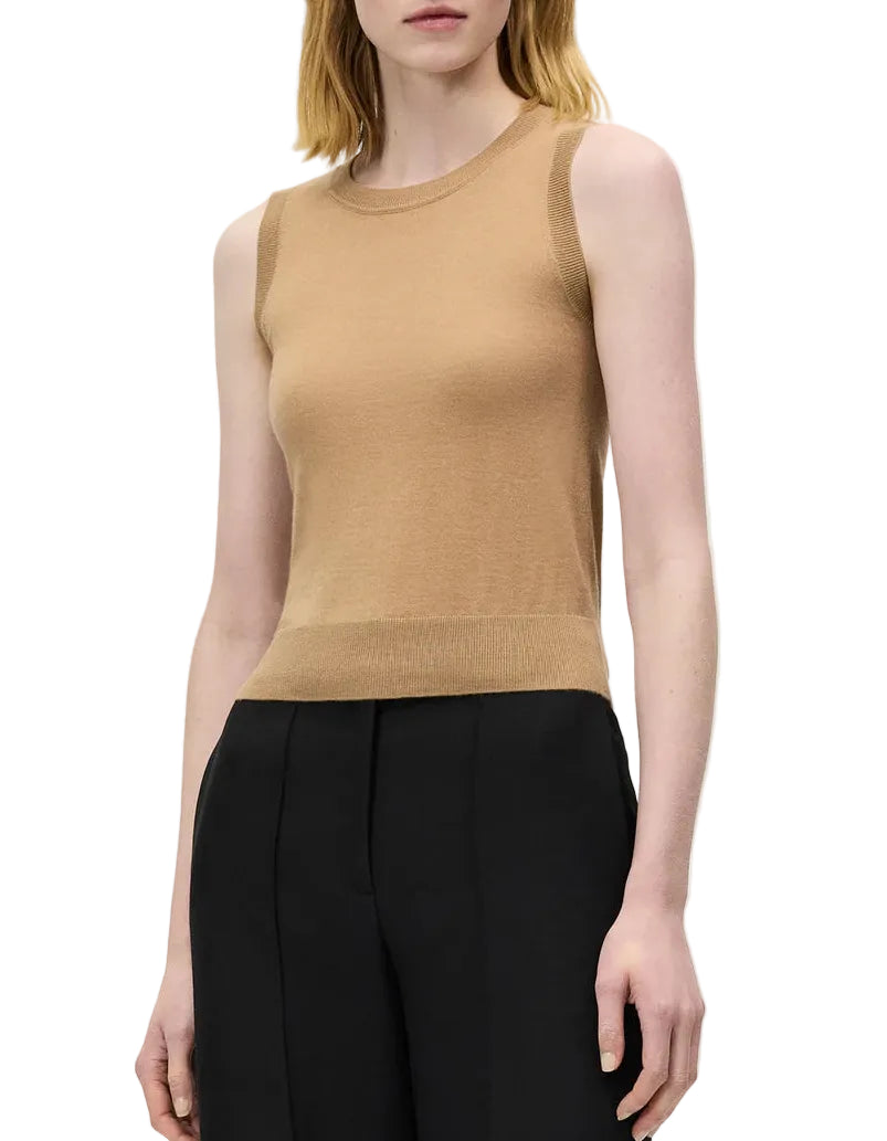 A woman wearing the sleeveless beige Ava Top by Adam Lippes and black trousers stands against a plain white background.