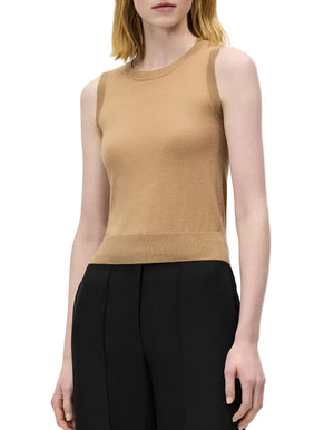 A woman wearing the sleeveless beige Ava Top by Adam Lippes and black trousers stands against a plain white background.