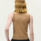 Person with shoulder-length, wavy blonde hair is shown from the back against a plain light background, wearing the Ava Top by Adam Lippes in a sleeveless beige cashmere silk blend and black pants.