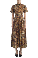 A person wears the Adam Lippes Leighton Dress—a short-sleeved, collared, ankle-length Italian cotton poplin style in a brown and black abstract animal print—paired with black shoes.