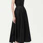 A woman wears the Adam Lippes Genevieve Dress—a sleeveless, button-up black shirtdress with a fitted waist and flared skirt—paired with black high-heeled sandals.