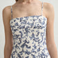A woman wearing the POSSE Rue Dress, a sleeveless linen-silk piece with thin straps, a square neckline, and a blue floral print on white.