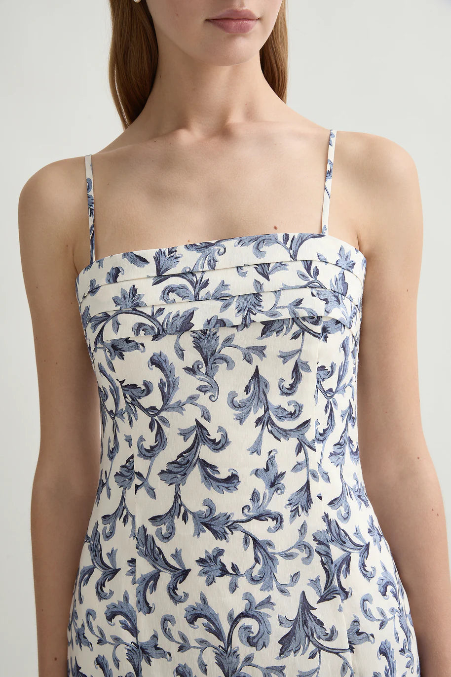 A woman wearing the POSSE Rue Dress, a sleeveless linen-silk piece with thin straps, a square neckline, and a blue floral print on white.