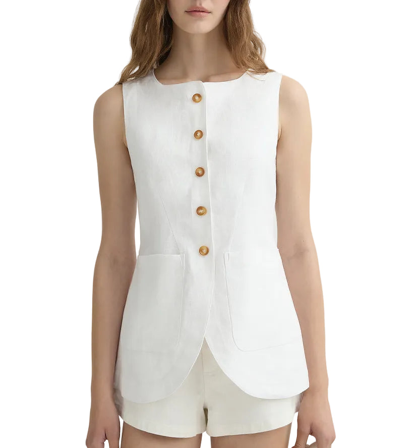 A woman wears the POSSE Emma Vest, a sleeveless white tailored vest with brown buttons, front pockets, and an adjustable back buckle, paired with white shorts. Her face is partially out of frame.