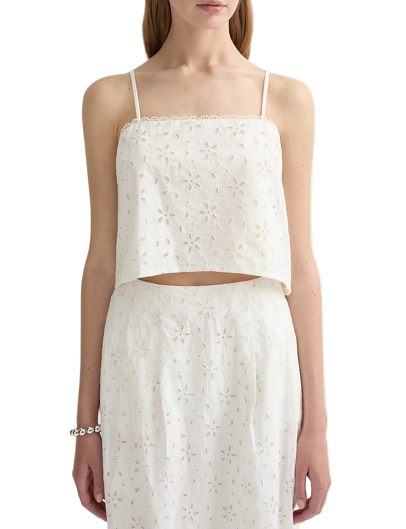 A woman wears the POSSE Salma Top, a white sleeveless embroidered crop top with a concealed zip, paired with a matching high-waisted skirt.