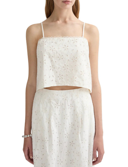 A woman wears the POSSE Salma Top, a white sleeveless embroidered crop top with a concealed zip, paired with a matching high-waisted skirt.