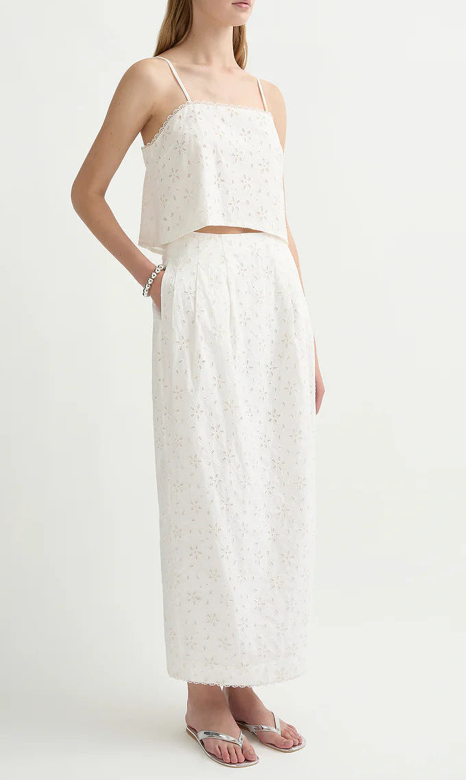 Wearing the POSSE Salma Top—an embroidered crop with adjustable straps—and a matching high-waisted, ankle-length floral skirt with pockets, she completes her look with sandals and keeps her hands in her skirt's pockets.