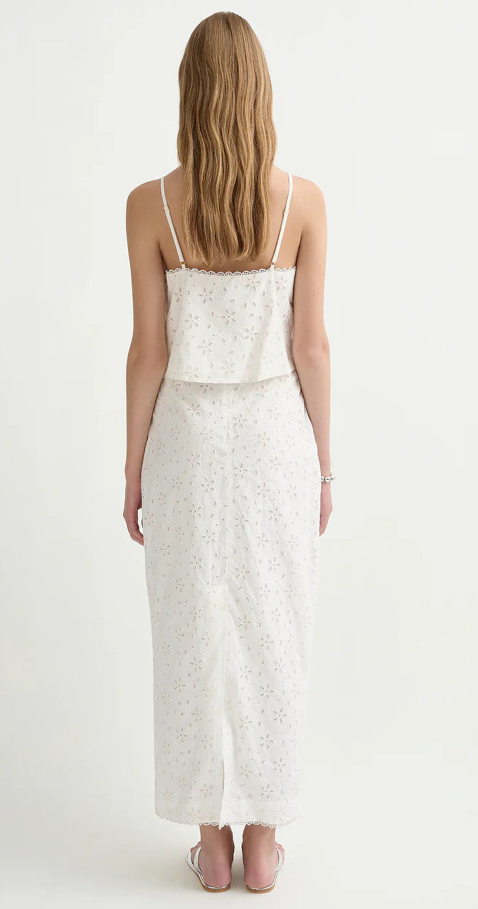 Woman with long, wavy hair wears the POSSE Salma Top, a white sleeveless piece with adjustable straps, paired with sandals and standing against a plain light background.