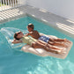 Two children are lying on a Sunnylife Luxe Lie-On Float, Ice Cream Sunday Multi in a pool. The girl is wearing a yellow swimsuit and sunglasses, and the boy is sporting blue swim trunks. They are enjoying a sunny day at their pool party.