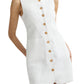 A woman wears the POSSE Emma Mini Dress—a sleeveless white linen mini dress featuring a high neckline, large front pockets, brown center buttons, and an adjustable back buckle for the perfect fit.